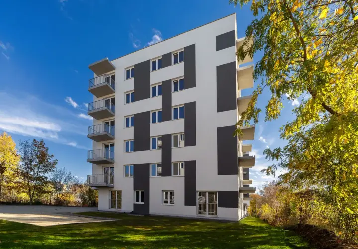 Nowoczesny budynek mieszkalny z balkonami i geometrycznym wzorem na elewacji, otoczony zielenią.